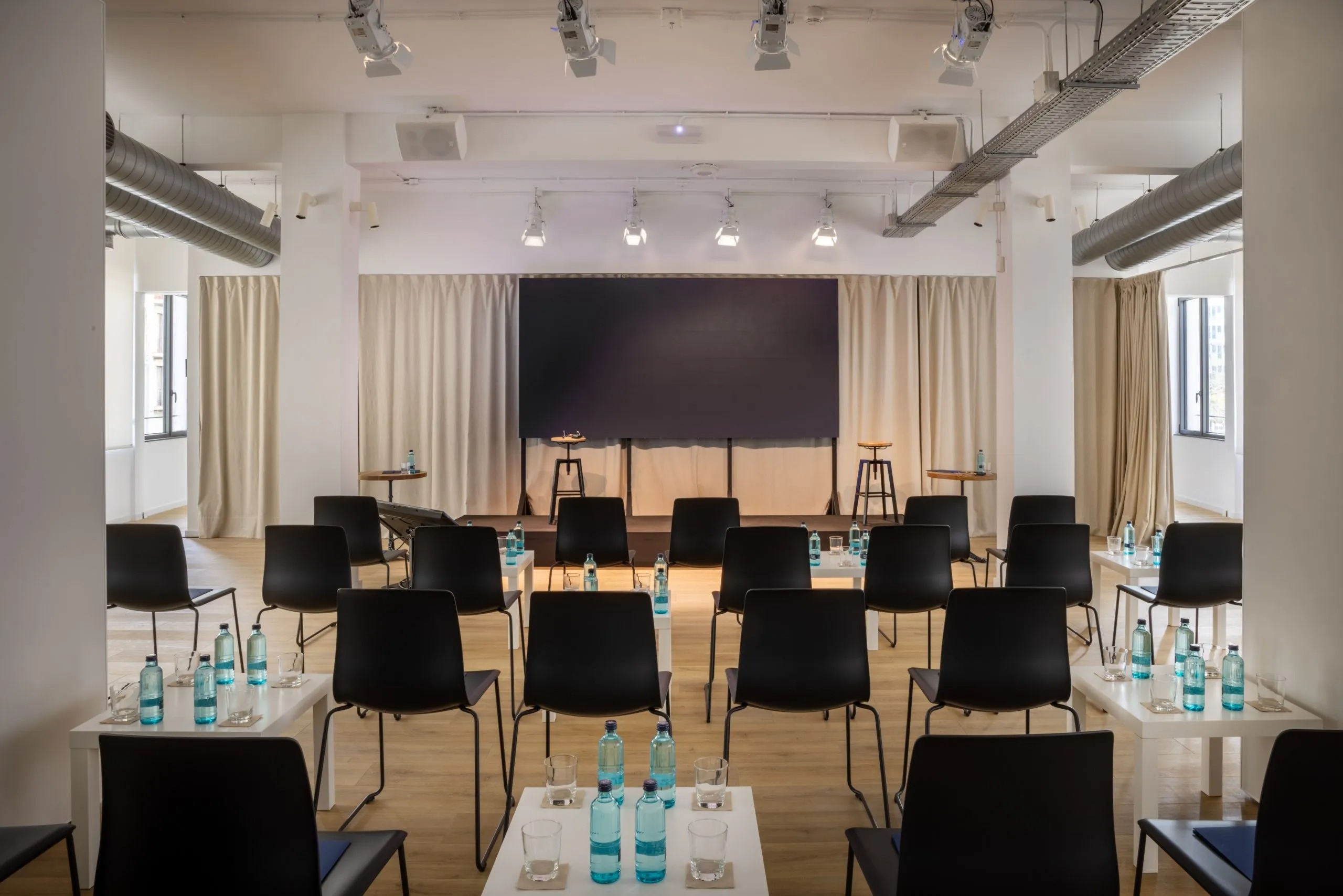 Espacios Para Eventos Corportativos En Barcelona sala con television para conferencias, sillas para asistentes y botellas de agua